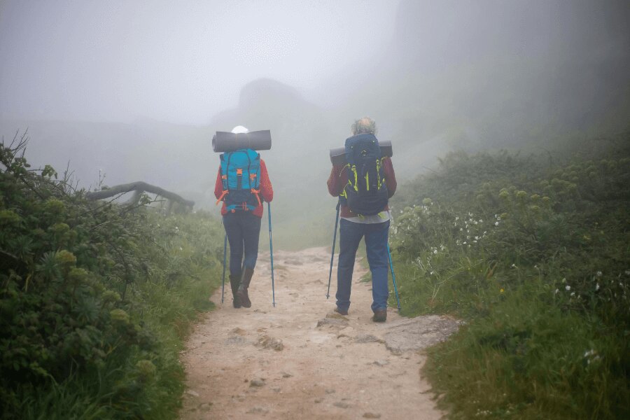 Pár v outdoorovém oblečení na treku v mlze. Zdroj: https://www.pexels.com/cs-cz/foto/dvojice-chuze-pesi-turistika-trava-7787435/