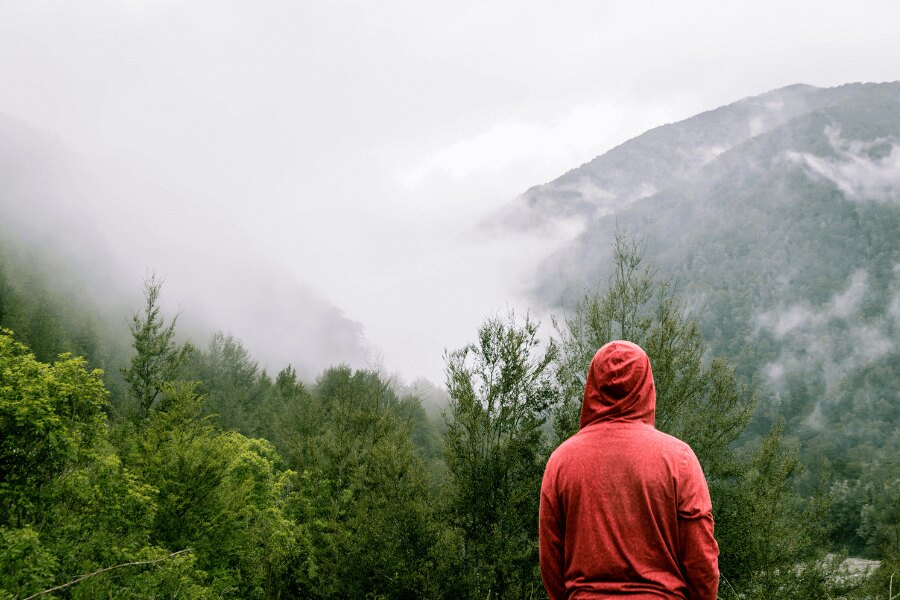 muž v červené mikině stojí na horách v dešti