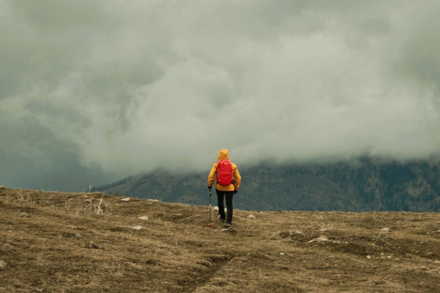 Muž ve žluté bundě trekuje v horách v dešti