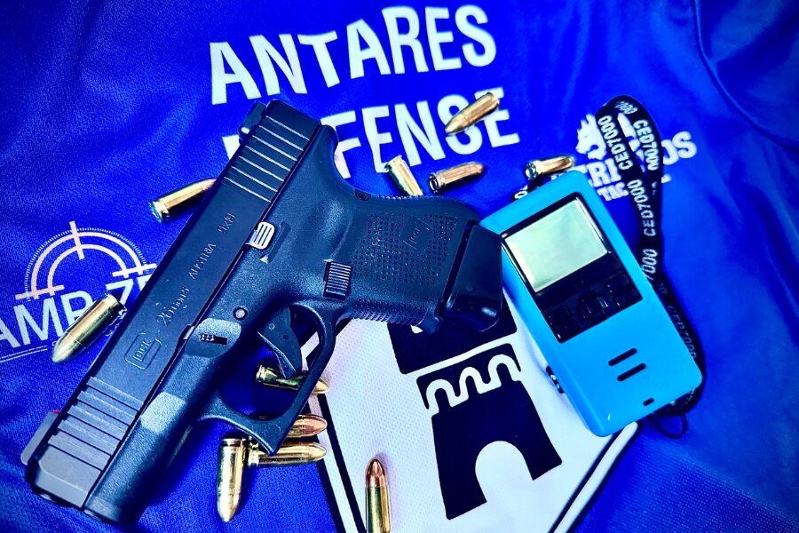 Tričko Antares Defense s logem, pistole Glock, náboje a měřič času. Zdroj: Facebook Antares Defense.