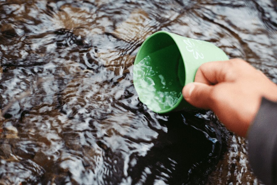 Nabírání vody v potoku do zeleného kelímku. Zdroj: https://www.pexels.com/cs-cz/foto/66090/